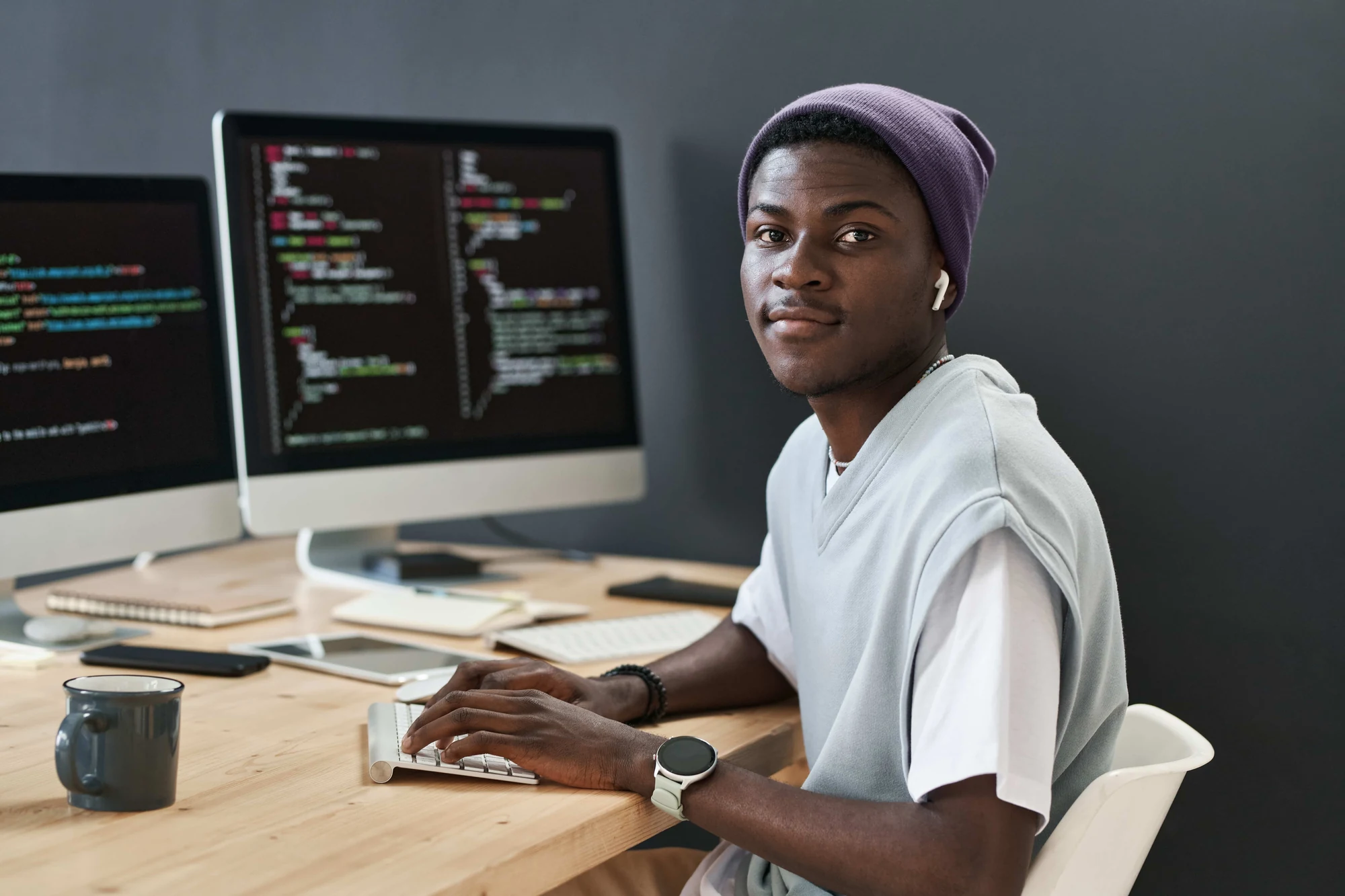 Développeur souriant devant deux écrans affichant du code, à son poste de travail