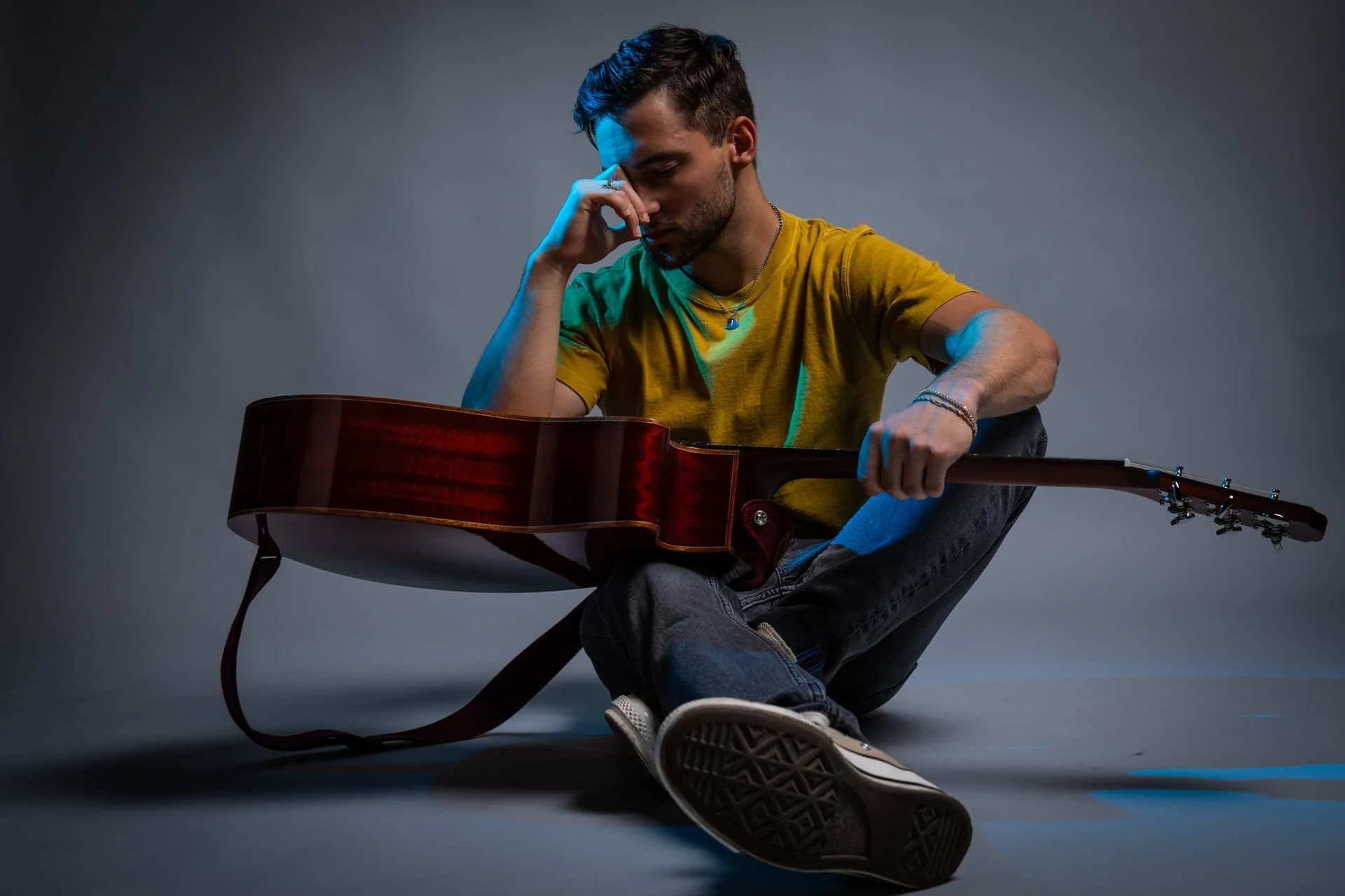 Musicien assis au sol avec sa guitare, portrait studio sur fond gris