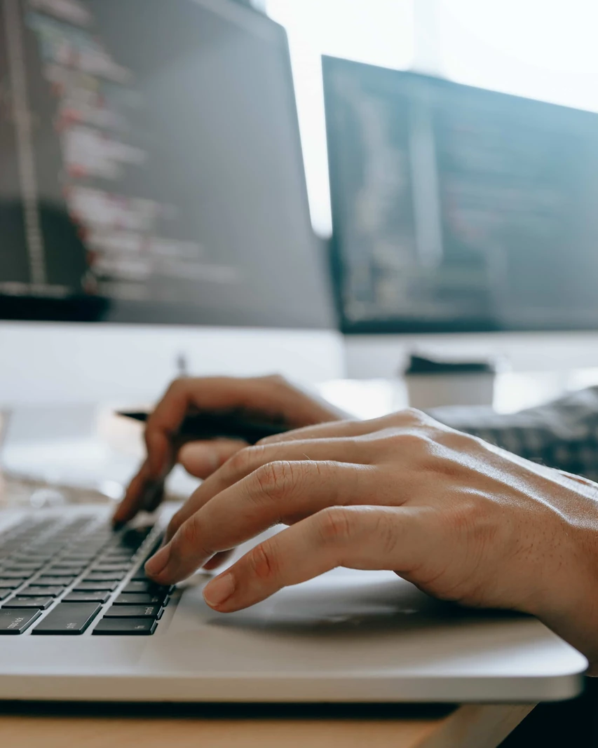 Mains d’un développeur tapant sur un ordinateur portable devant des écrans de code