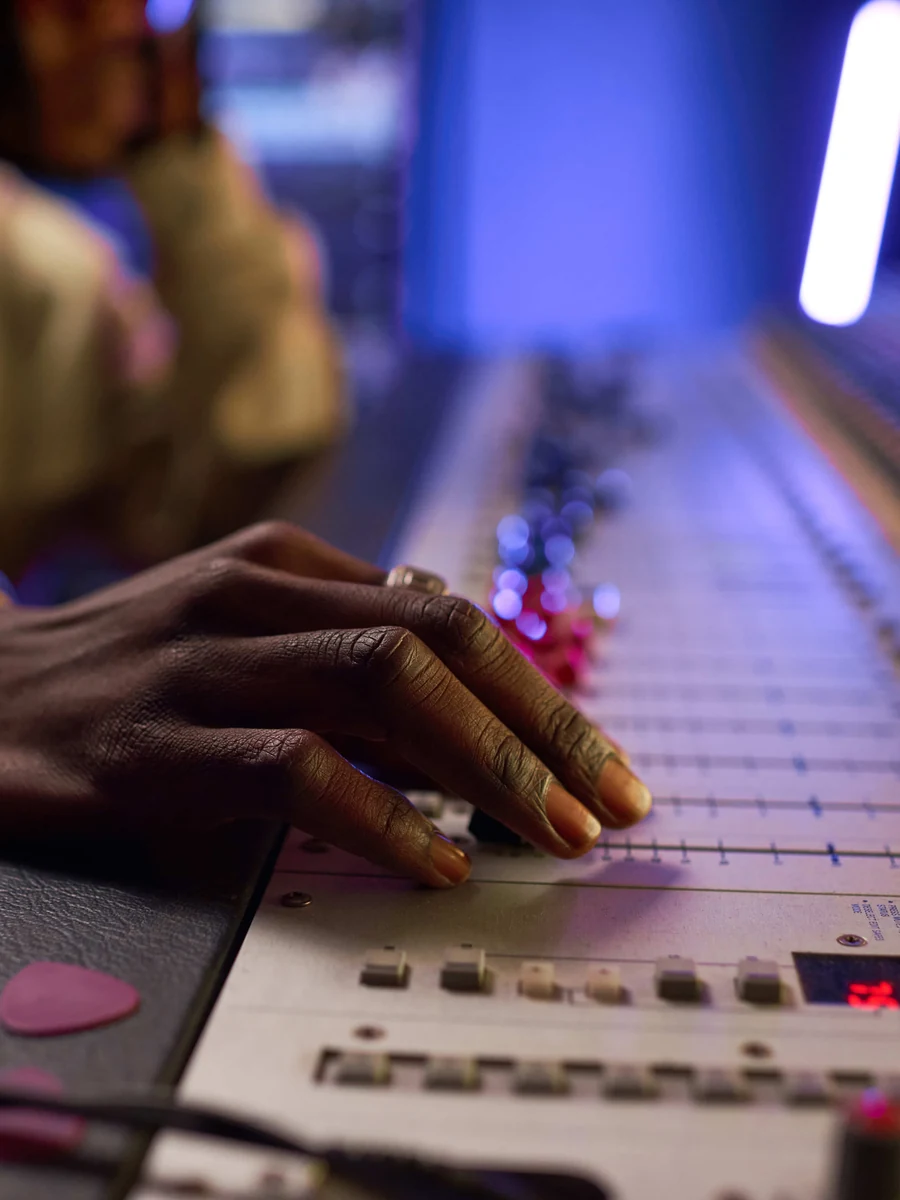 Main sur les faders d’une console de mixage, éclairage néon bleu