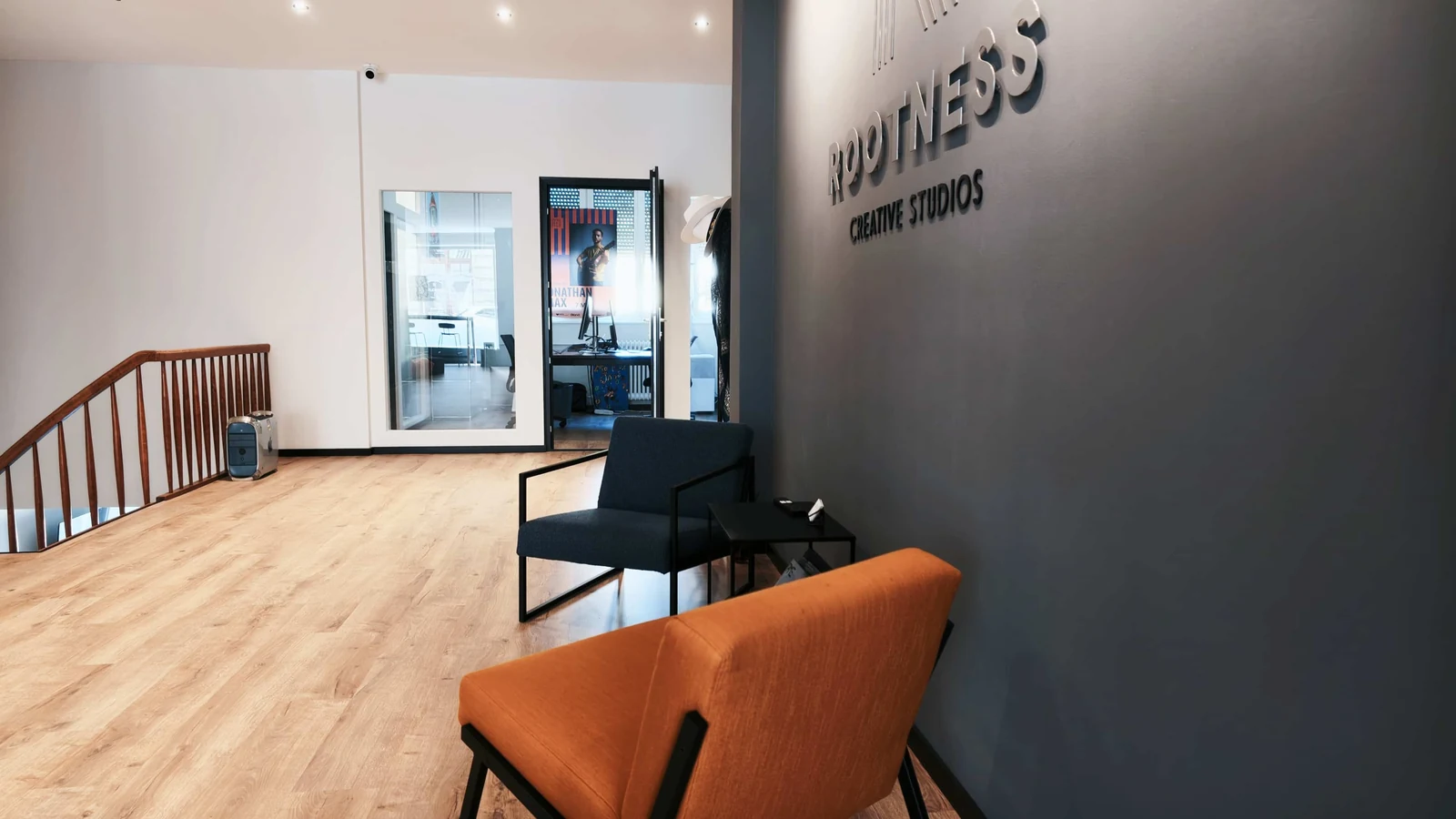 Accueil du studio Rootness à Montreux : parquet clair, fauteuils et mur gris au logo Rootness